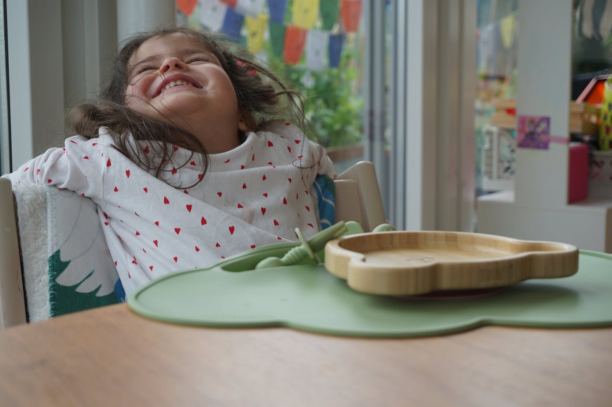 Mädchen lacht am Tisch vor einem Bambusteller