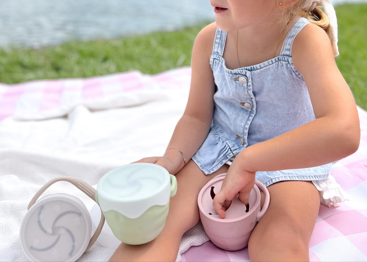 Kind auf der Picknickdecke mit Snackbox und Becher